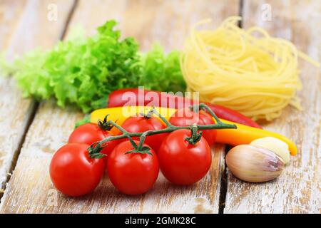 Selezione di ingredienti di cottura: Tagliatelle, pomodori ciliegini, spicchi d'aglio e peperoncini sulla superficie legnosa Foto Stock