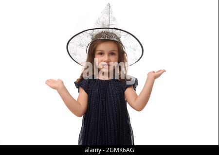 Concetto di Halloween. Ritratto isolato di bella ragazza strega con cappello mago, vestito in elegante abito carnevale, gesturing, tenendo una copia spac Foto Stock