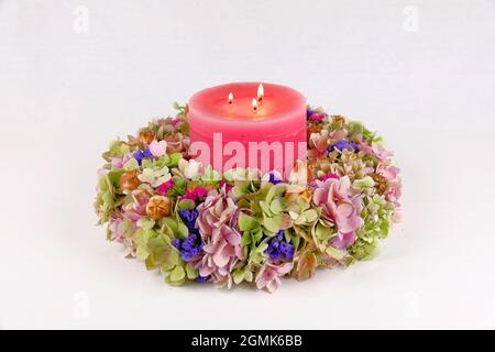 Una bella corona colorata con fiori su hydrangea e altri fiori e una candela rosa con tre luci Foto Stock