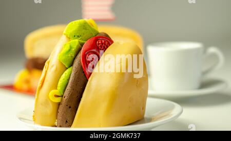 Pezzo della torta Burger, Madeira e torta stratificata di spugna di cioccolato, riempito con glassa ricoperta di glassa morbida e decorazioni di zucchero commestibile, torta i Foto Stock