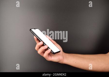 cornice di tenuta senza telefono cellulare con schermo bianco per messaggi o annunci su sfondo scuro, smartphone con schermo vuoto in mano dell'uomo Foto Stock