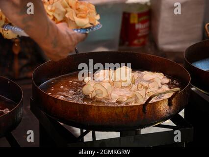 Un operaio in una cabina di cibo festival cuoca patatine fritte a nastro in grandi padelle di olio all'annuale Fiesta de Santa Fe a Santa Fe, New Mexico. Foto Stock