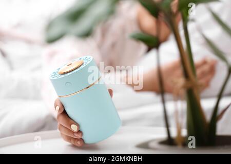 Donna con moderno umidificatore d'aria in camera da letto, primo piano Foto Stock