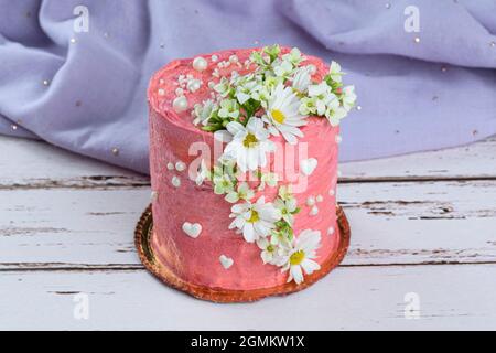 Torta al cioccolato ricoperta di crema di burro rosa. Decorato con cuori bianchi, perle e fiori. Sullo sfondo un tessuto lilla. Foto Stock