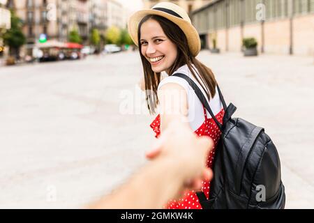 Gioiosa donna alla moda che tiene la mano del ragazzo in città Foto Stock