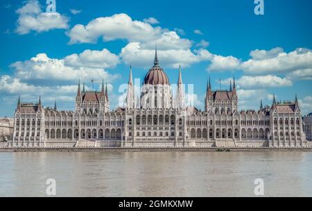 Vista estiva del Parlamento ungherese costruito in stile neogotico lungo il Danubio con perfetta simmetria con cielo blu nuvoloso Foto Stock