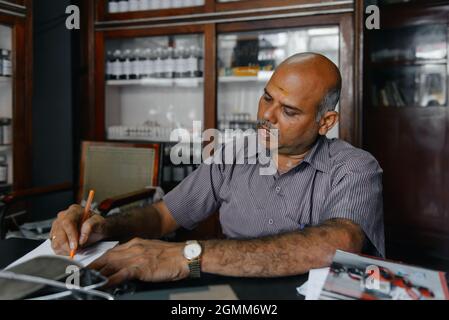 Aranmula, India - 5 dicembre 2015: Farmacia Ayurveda reale in Kerala con medico. Trattamento tradizionale della malattia in Asia. Scaffali con bottiglie e. Foto Stock