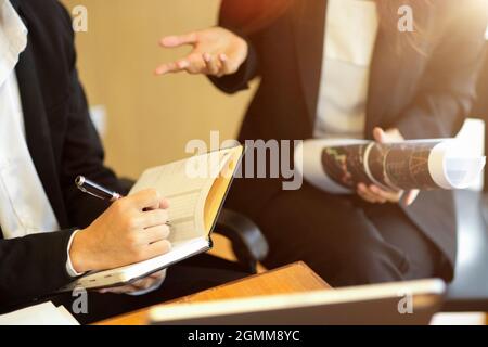 Scatto corto della donna d'affari dell'esecutivo seduta alla scrivania che dà il consiglio di strategia di affari al suo assistente giovane. Uomo d'affari che prende appunti su a personale Foto Stock