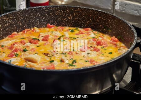 Il pesce branzino con pomodori finocchi e basilico viene fritto in padella sul fornello a gas. Foto Stock