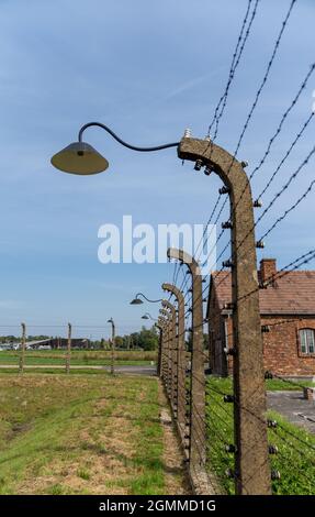 Auschwitz, Polonia - 15 settembre 2021: Recinzione di filo spinato e lanterne con casa di guardia sullo sfondo al campo di concentramento di Auschwitz Foto Stock