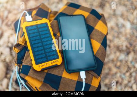 Power Bank carica lo smartphone tramite un cavo USB. Vista dall'alto, primo piano. Ciottoli sullo sfondo. Spazio di copia. Concetto di gadget moderni. Foto Stock