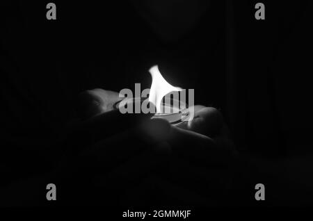 Colpo bianco e nero delle mani del maschio che tiene una candela che brucia in t Foto Stock