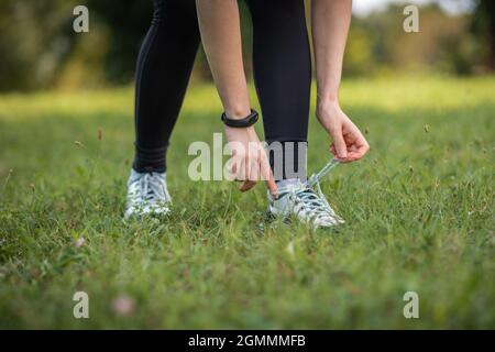 Donna in abbigliamento sportivo che lega le scarpe alle sneakers. Primo piano delle mani con smartwatch e scarpe. Concetto di sport e fitness. Foto Stock