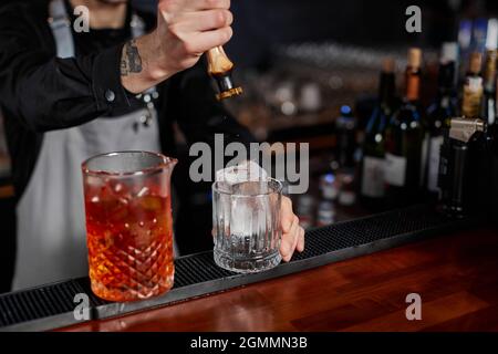 il barman in grembiule versa un cocktail vecchio stile in un bicchiere Foto Stock