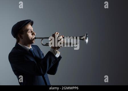 Giovane musicista maschile che suona tromba su sfondo grigio Foto Stock