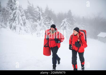 Paramedici dal servizio di soccorso in montagna che corre all'aperto in inverno in foresta. Foto Stock