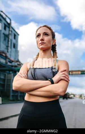 Donna sportiva con braccia incrociate in posa davanti ad una fabbrica Foto Stock