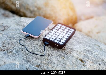 Portatile alimentato solare usb carica il telefono e si trova su una roccia sulla spiaggia. Energia alternativa. Eco. Foto Stock
