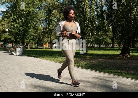 Giovane e giovane contemporanea, oltre a una donna africana in abbigliamento sportivo, jogging nel parco la mattina di sole Foto Stock