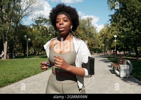 Giovane e donna attiva di più dimensioni che ascolta la musica mentre jogging nel parco Foto Stock