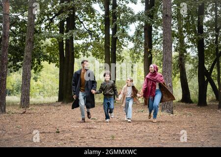 Felice famiglia araba che tiene le mani mentre corre nel parco Foto Stock