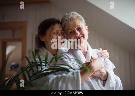 Felice madre anziana in accappatoio con la figlia adulto che abbraccia al chiuso a casa, concetto di auto-cura. Foto Stock