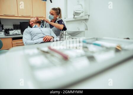 Dentista femminile caucasica che opera su un cliente maschile seduto in sedia medici in sala clinica Foto Stock