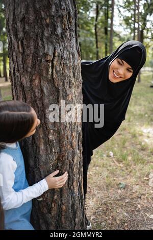 Madre musulmana in hijab guardando la figlia vicino albero nel parco Foto Stock