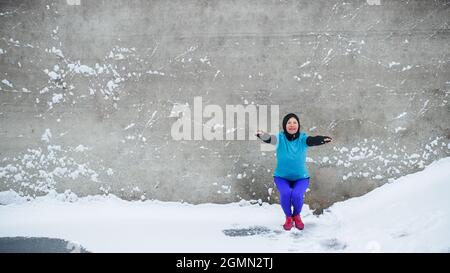 Vista frontale di una donna anziana attiva all'aperto in inverno nevoso, facendo squats. Spazio di copia. Foto Stock
