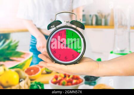 Mano della donna che tiene un orologio in una cucina. Concetto di digiuno intermittente. Spazio di copia vuoto per il testo dell'editor. Foto Stock