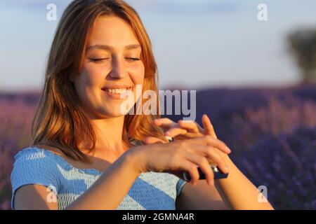 Donna felice che applica crema moisturzer in mani in campo lavanda al tramonto Foto Stock