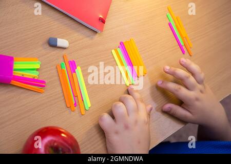 Le mani ravvicinate dello studente sono contate come bastoni multicolore. Uno scolaro svolge un compito sul posto di lavoro. Il concetto di educazione dei bambini, di insegnamento delle conoscenze, delle competenze e delle abilità. Foto Stock