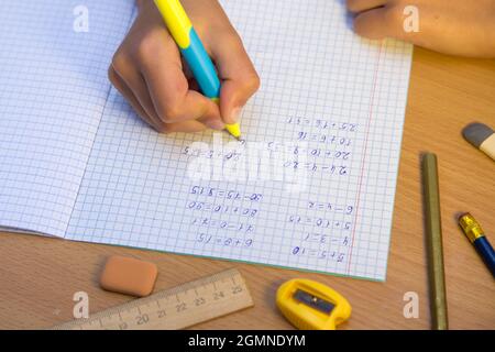 La mano della pupilla in primo piano scrive con una penna a sfera in un notebook. Uno scolaro svolge un compito sul posto di lavoro. Il concetto di educazione dei bambini, di insegnamento delle conoscenze, delle competenze e delle abilità. Foto Stock