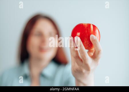 Ritratto di una giovane donna allegra in una t-shirt bianca che mangia mela rossa su sfondo grigio. Dieta sana di nutrizione. Snack alla vitamina Apple. Foto Stock