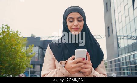 Giovane musulmana in messaggi hijab su smartphone fuori Foto Stock