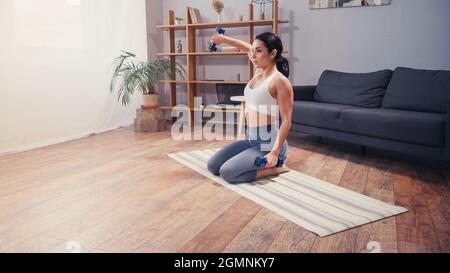 Atletica sportiva pratica con manubri sul tappeto da fitness a casa Foto Stock