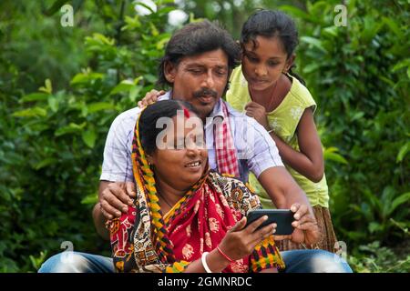 3 genitori rurali indiani e figlia che guardano il film in campo agricolo Foto Stock