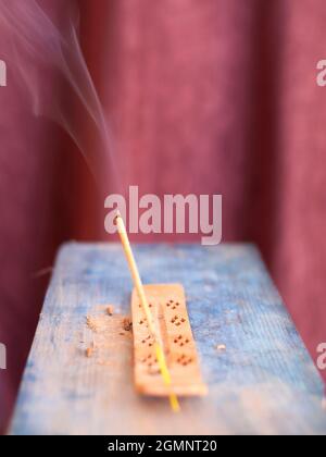 bastone di incenso illuminato con filo di fumo con sfondo scuro su base di azzurro cielo chiaro Foto Stock