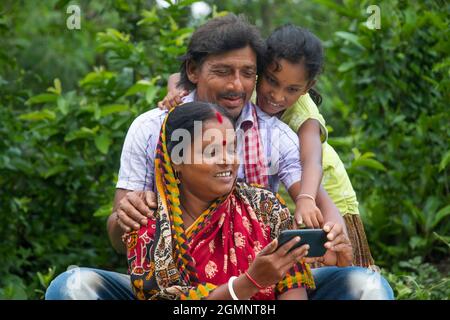 3 genitori rurali indiani e figlia che guardano il film in campo agricolo Foto Stock