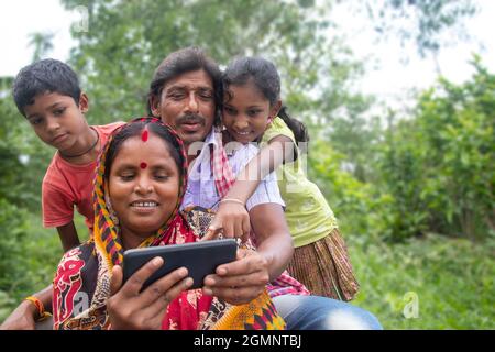 I genitori rurali indiani ed i loro due bambini che guardano il film in campo agricolo Foto Stock