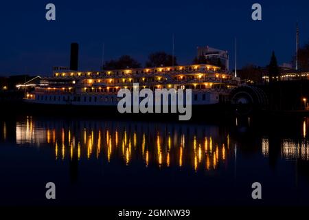 Delta King Hotel nella vecchia Sacramento di notte, vicino a Natale, vista dall'altra parte del fiume Sacramento, con luci di vacanza che si riflettono sul fiume, Foto Stock