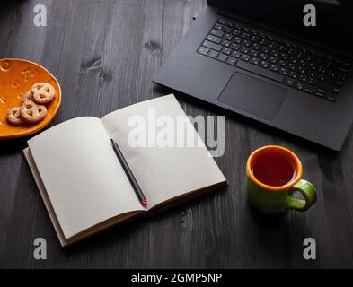Tazza di caffè nero su sfondo di legno scuro, laptop aperto e notebook nelle vicinanze. Vista dall'alto Foto Stock