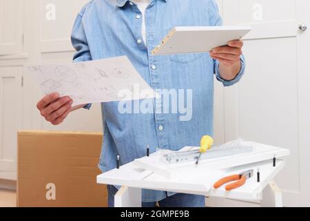 Primo piano delle istruzioni di lettura dell'uomo e mettere insieme i mobili di autoassemblaggio a casa Foto Stock