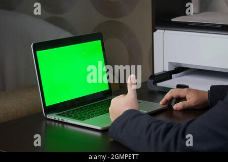 Un uomo lavora a un computer portatile con uno schermo verde. Mostra un gesto con il pollice verso l'alto. Chromakey. Foto Stock