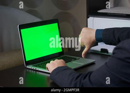 Un uomo lavora a un computer portatile con uno schermo verde. Mostra un gesto del pollice verso il basso. Chromakey. Foto Stock