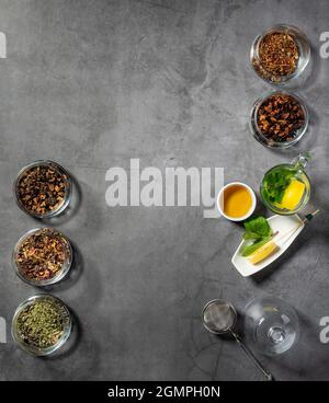 Layout creativo con tè, tè verde, tè nero e vari tipi di frutta e tisane su sfondo di pietra scura. Posa piana. Foto Stock