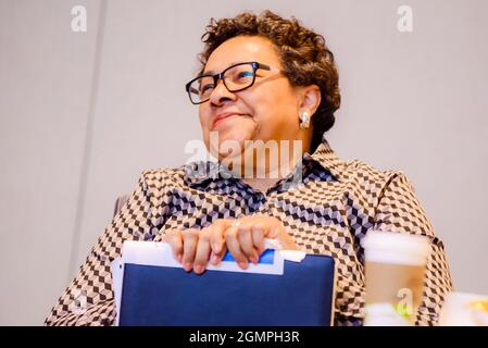 Donna più anziana afroamericana vestita professionalmente ridendo mentre si siede ad un tavolo Foto Stock