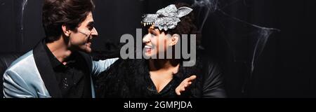 felice african american donna in maschera lupo parlare con l'uomo in halloween trucco, banner Foto Stock