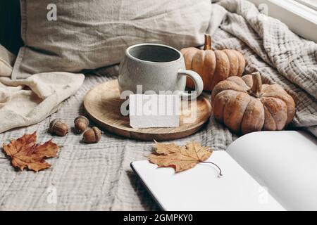 Accogliente colazione autunnale mattina ancora vita. Tazza di caffè caldo, tè figlio piatto di legno vicino alla finestra. Mockup biglietto da visita vuoto. Autunno, concetto di Thanksgiving Foto Stock