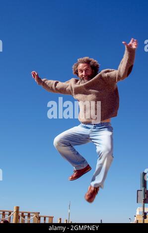 un uomo anziano sorridente di 50-60 anni con capelli ricci è nell'aria per un salto e solleva le braccia Foto Stock